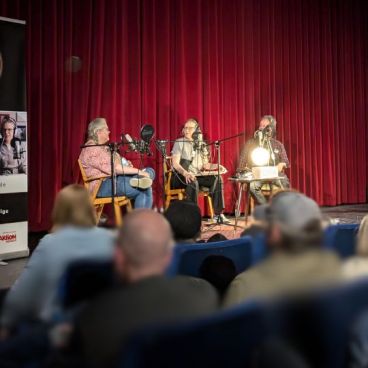 Drei Menschen auf der Bühne bei der AUfnahme eines LIve-Podcasts vor Publikum